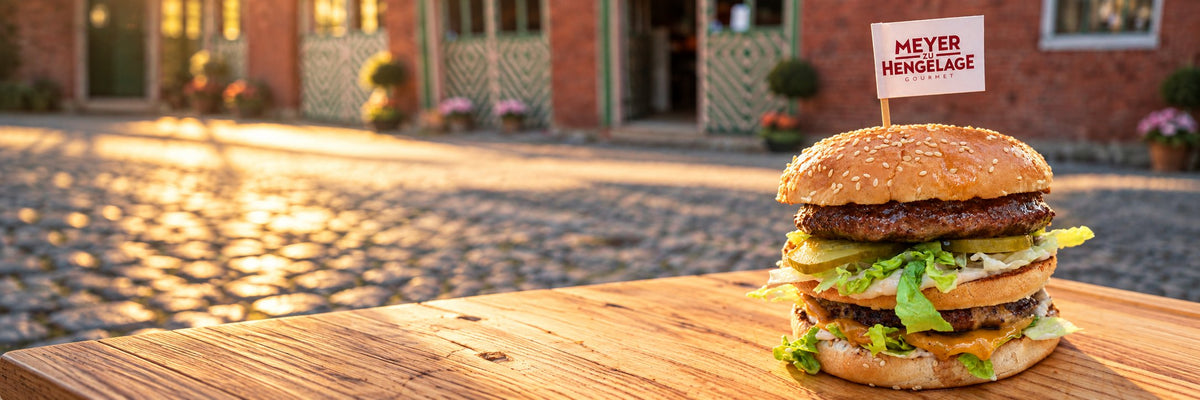 Doppelter Burger mit Meyer-zu-Hengelage-Fähnchen auf dem Holzbrett vor dem Hofladen
